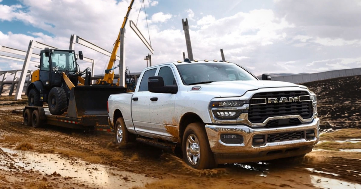 White Ram 4x4 pickup truck rental driving through a muddy jobsite with heavy equipment in the background.