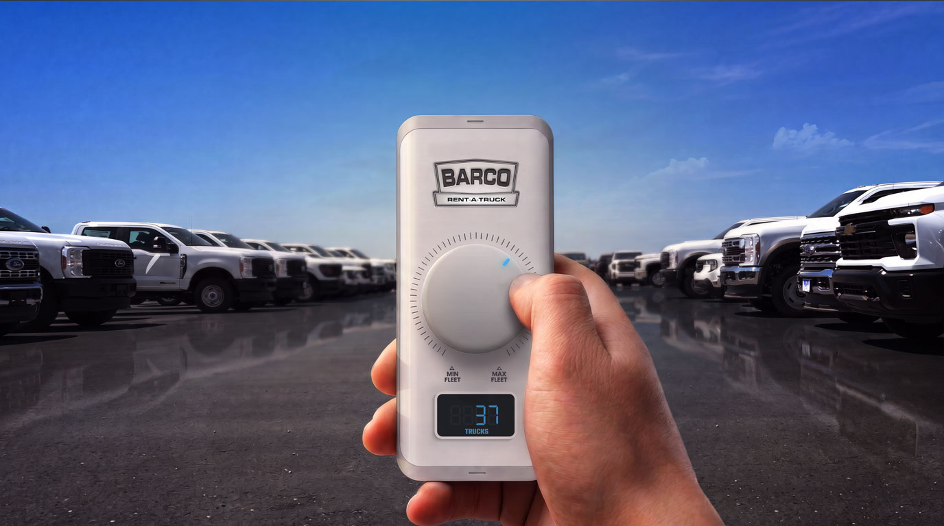 Hand holding a Barco fleet control device in front of rows of white rental work trucks.